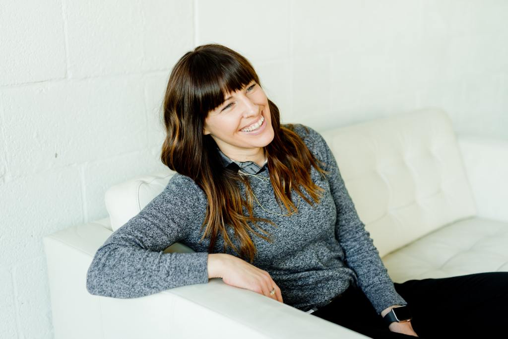 Image of female confident hypnotist, smiling, sitting on a white sofa.
 
